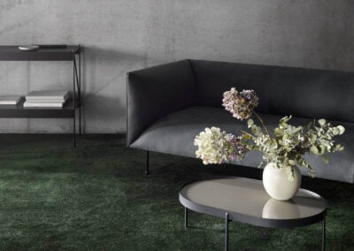 En stue med mørkegrønt gulvtæppe fra BT gulve. Grå sofa og sofabord med blomster på